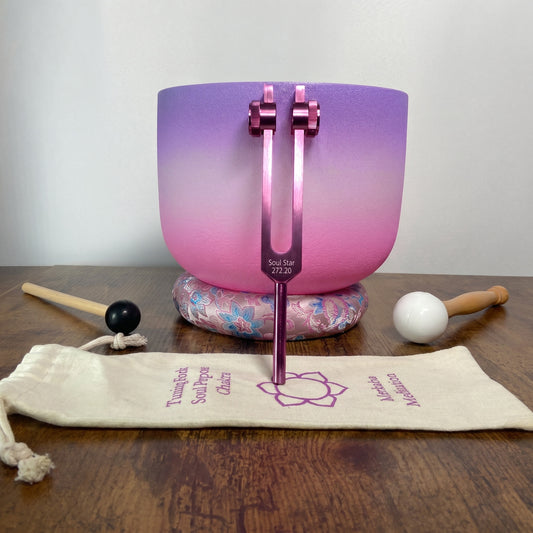 a purple and pink crystal bowl, a wooden stick, a black and white ball, and a beige bag with text on it, all arranged on a wooden surface.