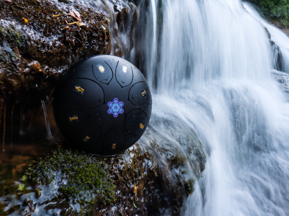 Steel tongue drum placed beside a waterfall for meditation, sound healing, relaxation, and holistic wellness.