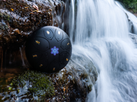 Steel tongue drum placed beside a waterfall for meditation, sound healing, relaxation, and holistic wellness.