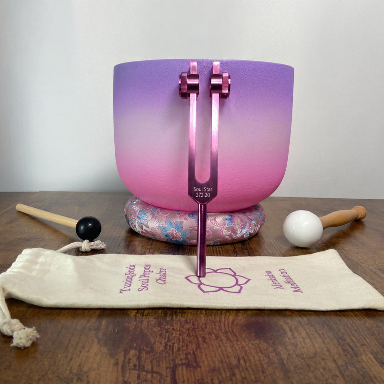a purple and pink crystal bowl, a wooden stick, a black and white ball, and a beige bag with text on it, all arranged on a wooden surface.