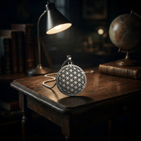 Black and silver Flower of Life charm necklace styled on a desk