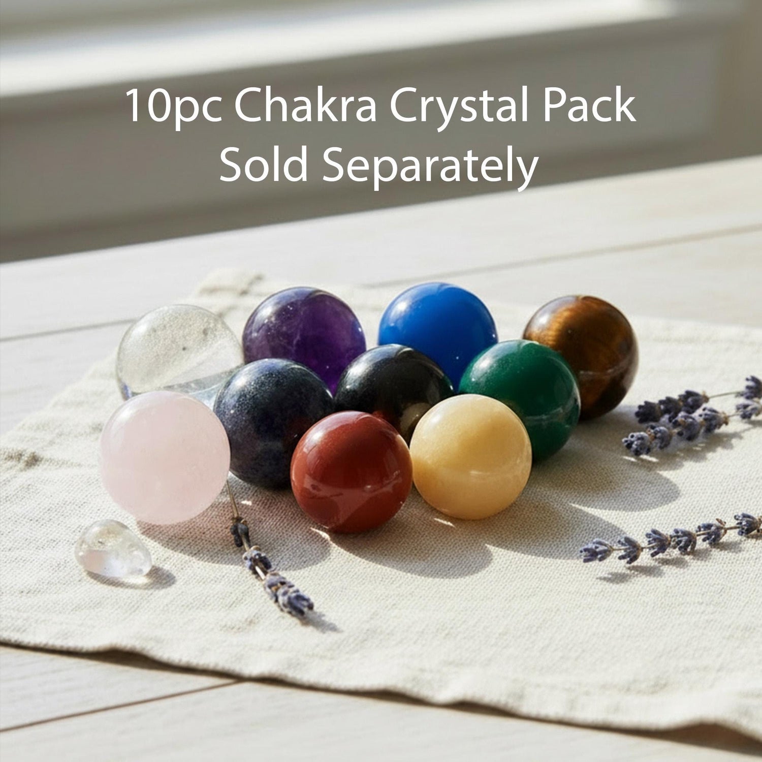 A collection of colorful crystal balls and gemstones arranged on a white cloth, with some lavender flowers visible in the background.