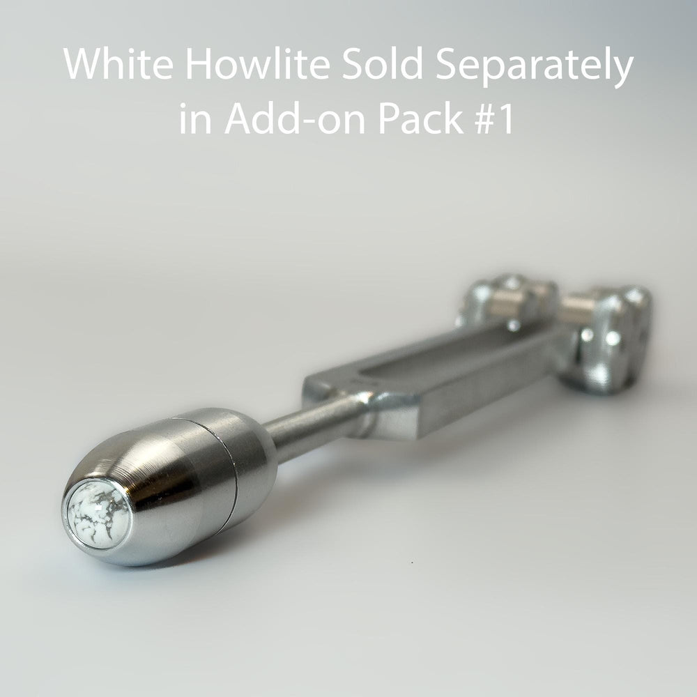 A close-up view of a silver-colored metal object, possibly a tool or device, with a text overlay that reads "White Howlite Sold Separately in Add-on Pack #1".