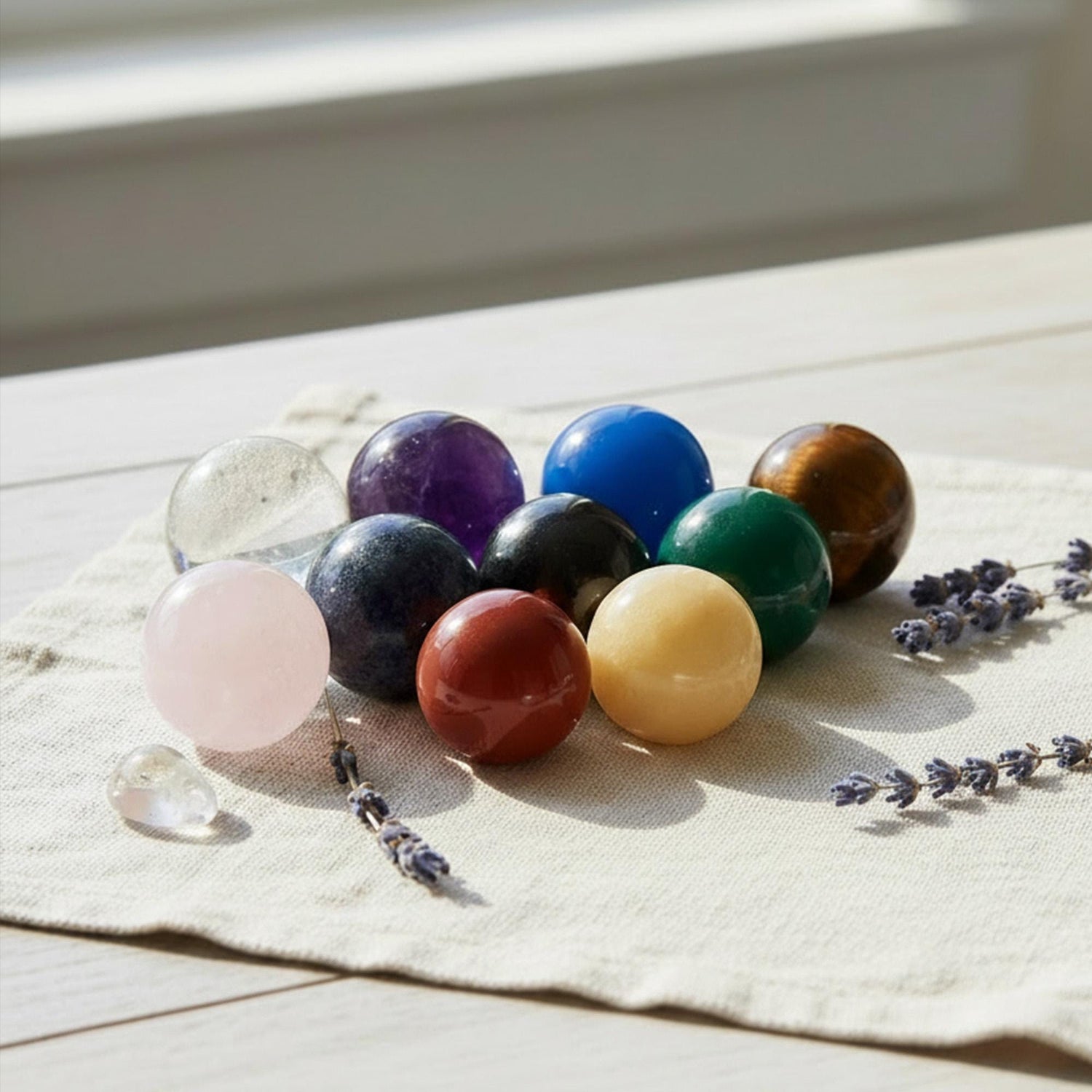 a collection of colorful gemstones and crystals arranged on a white cloth, with some lavender flowers scattered around.