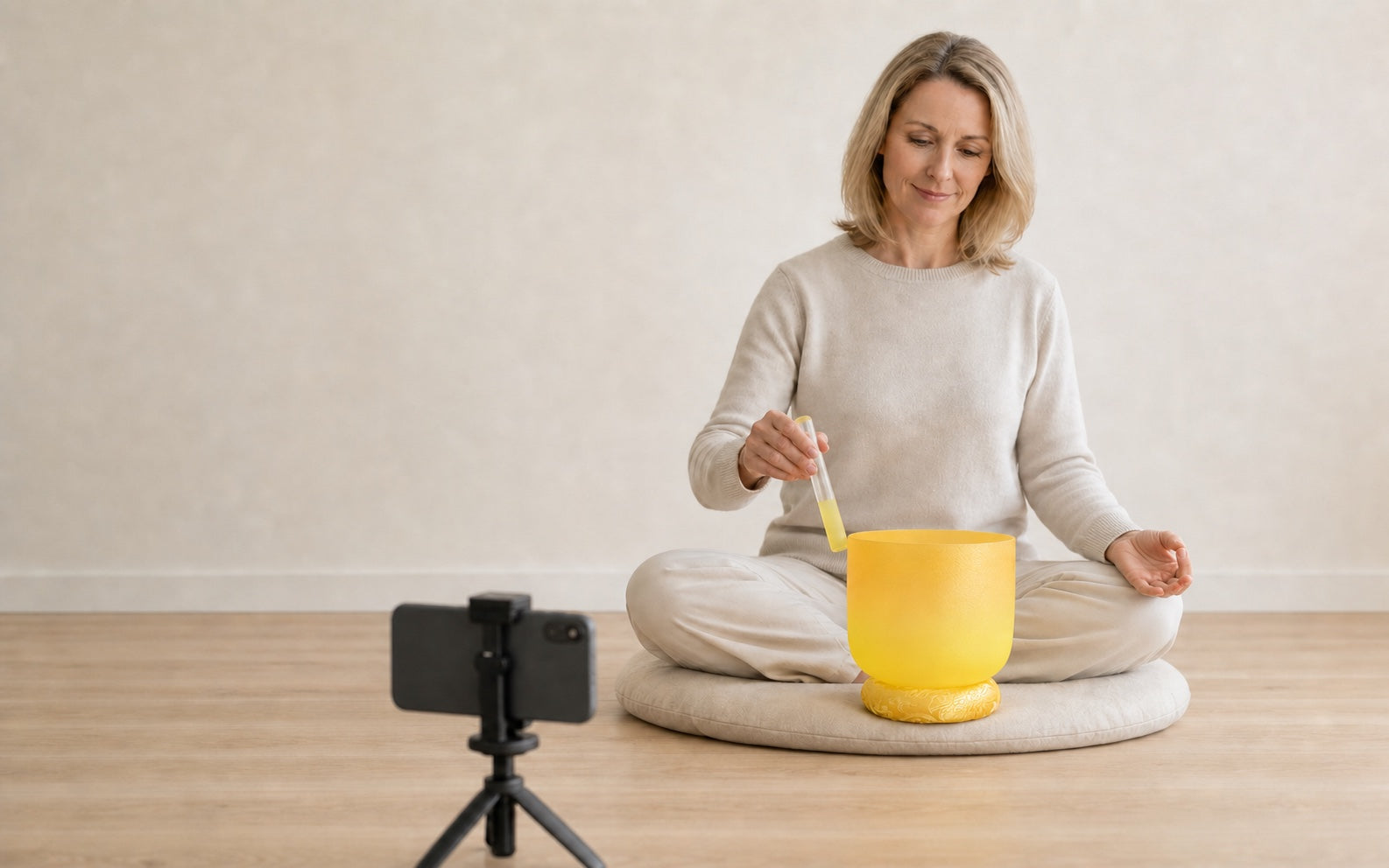 Sound healing practitioner recording a simple crystal singing bowl demonstration with a peaceful smile and meditation mudra